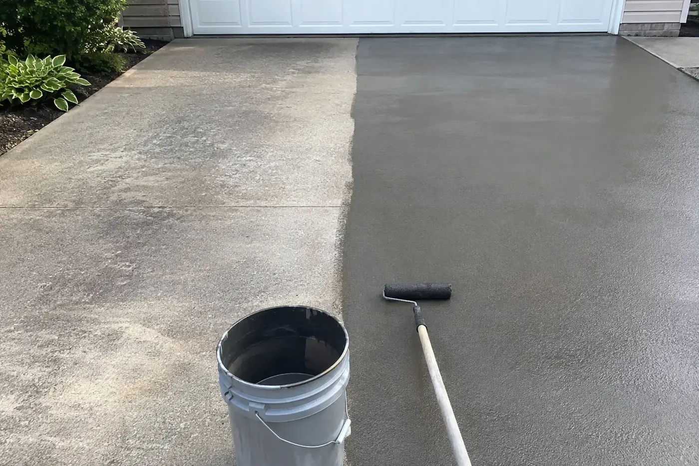 Concrete driveway half sealed, roller and sealer bucket at the edge in Avon, IN